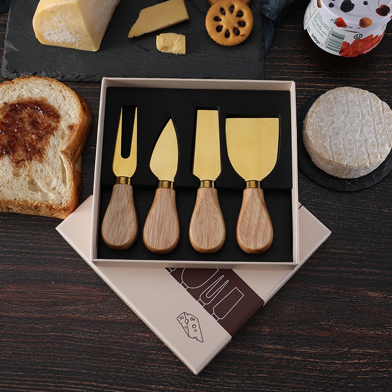 Gold cheese knife set in open box: fork, wedge and spreader blades with wooden handles