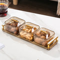 Set of glass containers with gold lids on a tray, filled with nuts, on a white surface.
