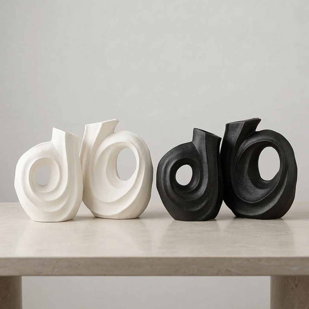 Two white and two black abstract sculptures on a light gray surface with a neutral background