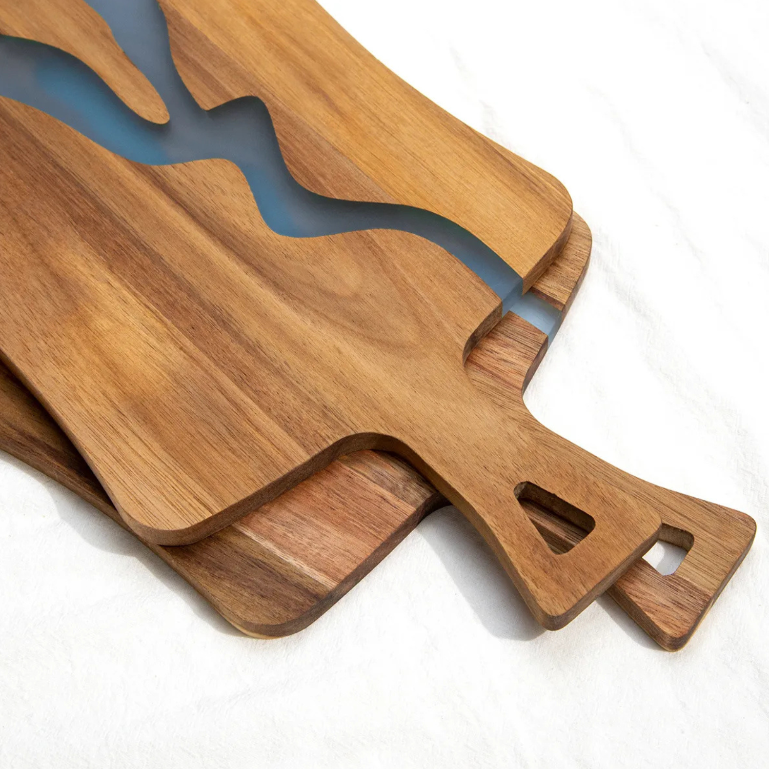 Acacia wood cutting board close-up with blue epoxy river and end grip handle