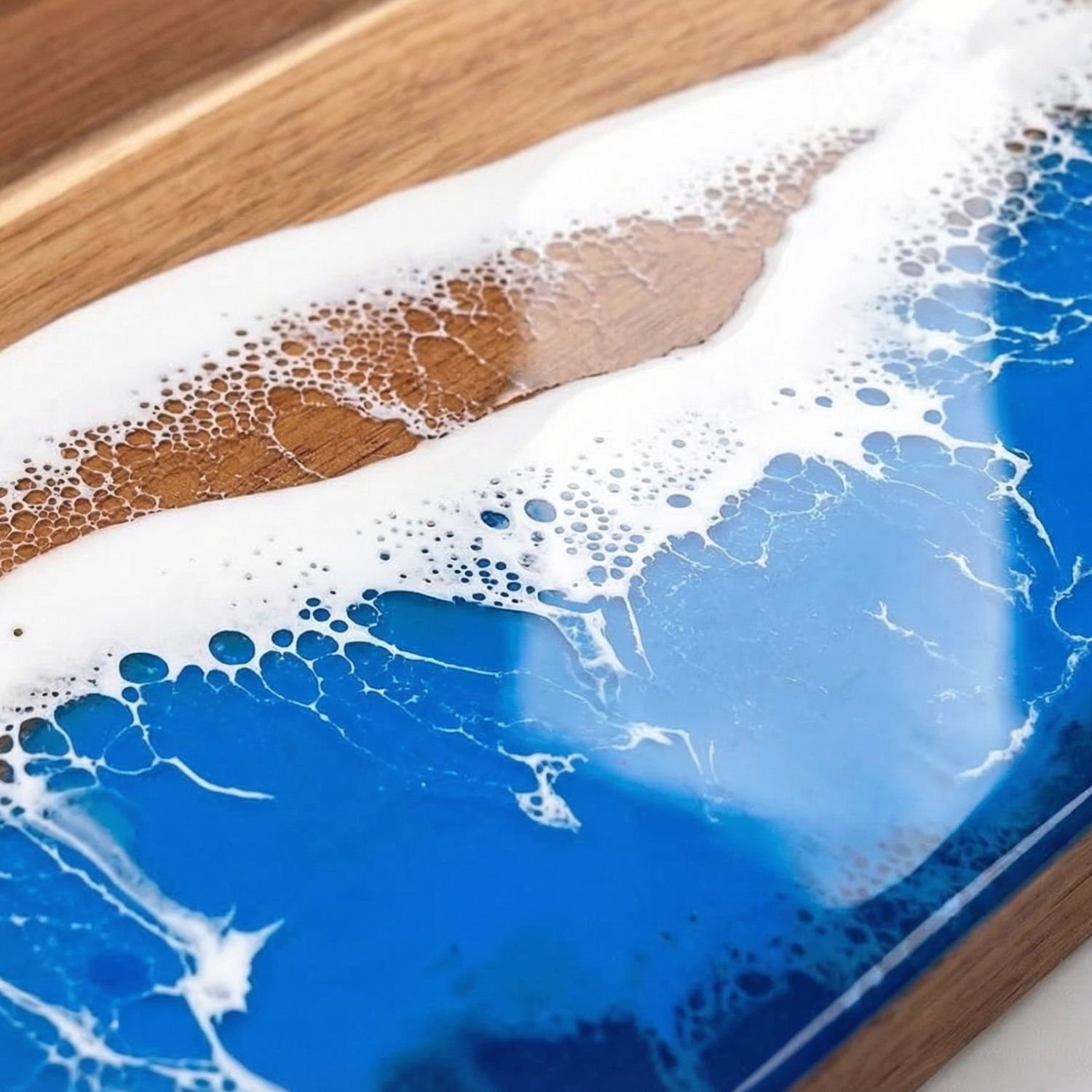 Close-up of ocean wave resin edge: blue epoxy with white bubbles and brown wood line