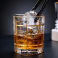 Glass of whiskey with ice cube and tongs on a dark background