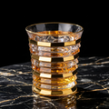 Ribbed crystal rocks glass with stacked gold bands and gold rim, showing faceted texture.
