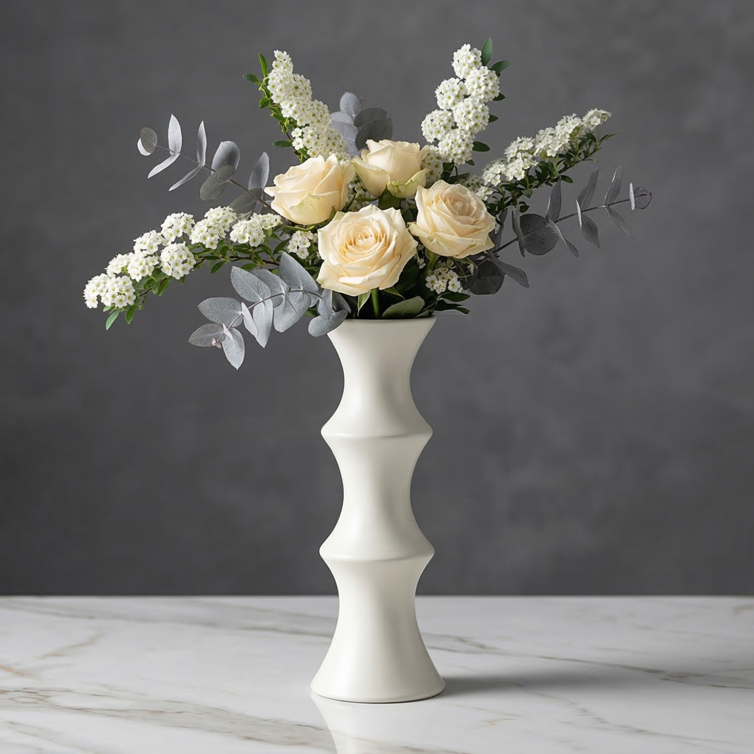 White vase with a bouquet of white and beige roses on a marble surface with a dark background