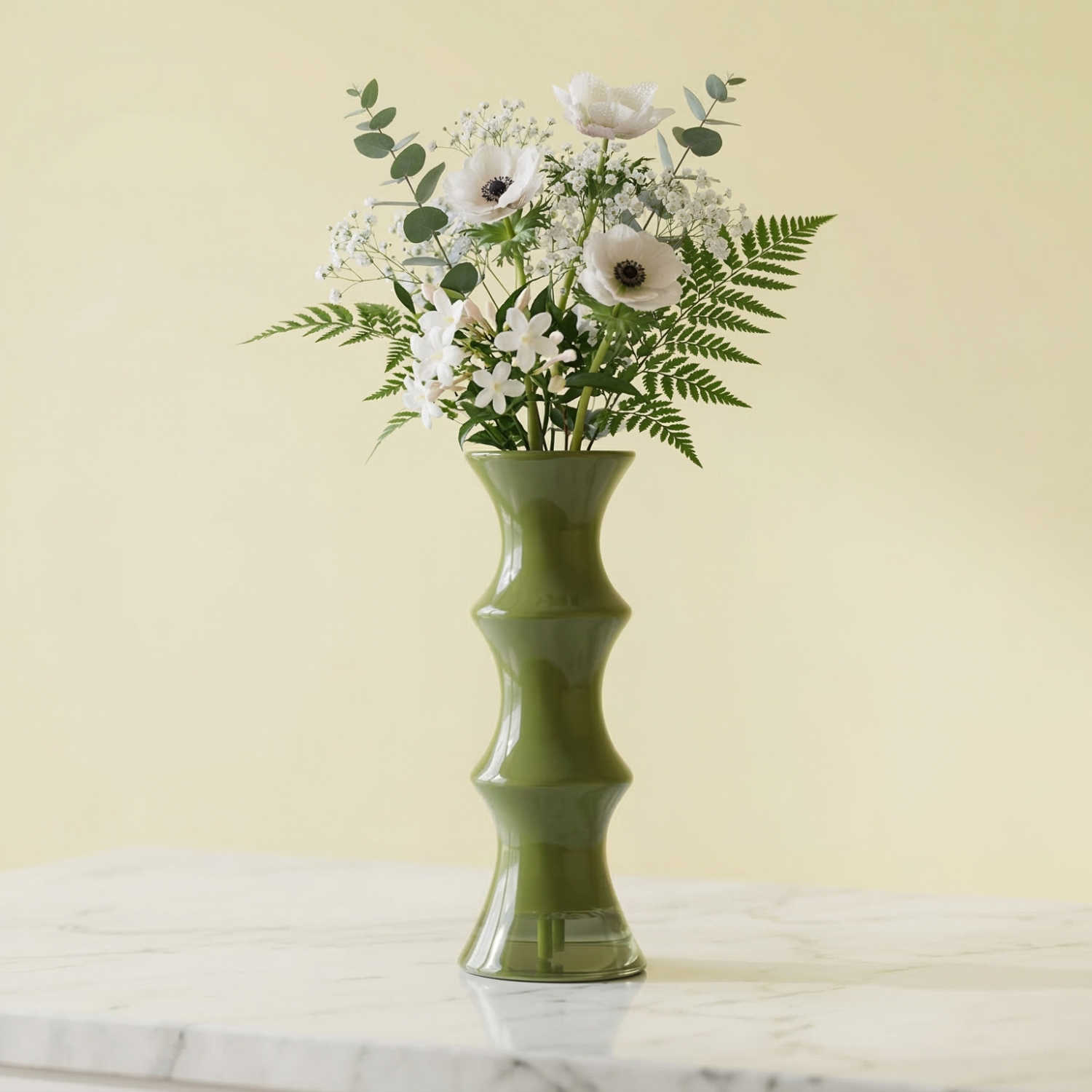 Green vase with a bouquet of flowers on a marble surface against a light yellow background
