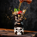 Skull tiki mug in black ceramic with white face, cocktail pouring into the top