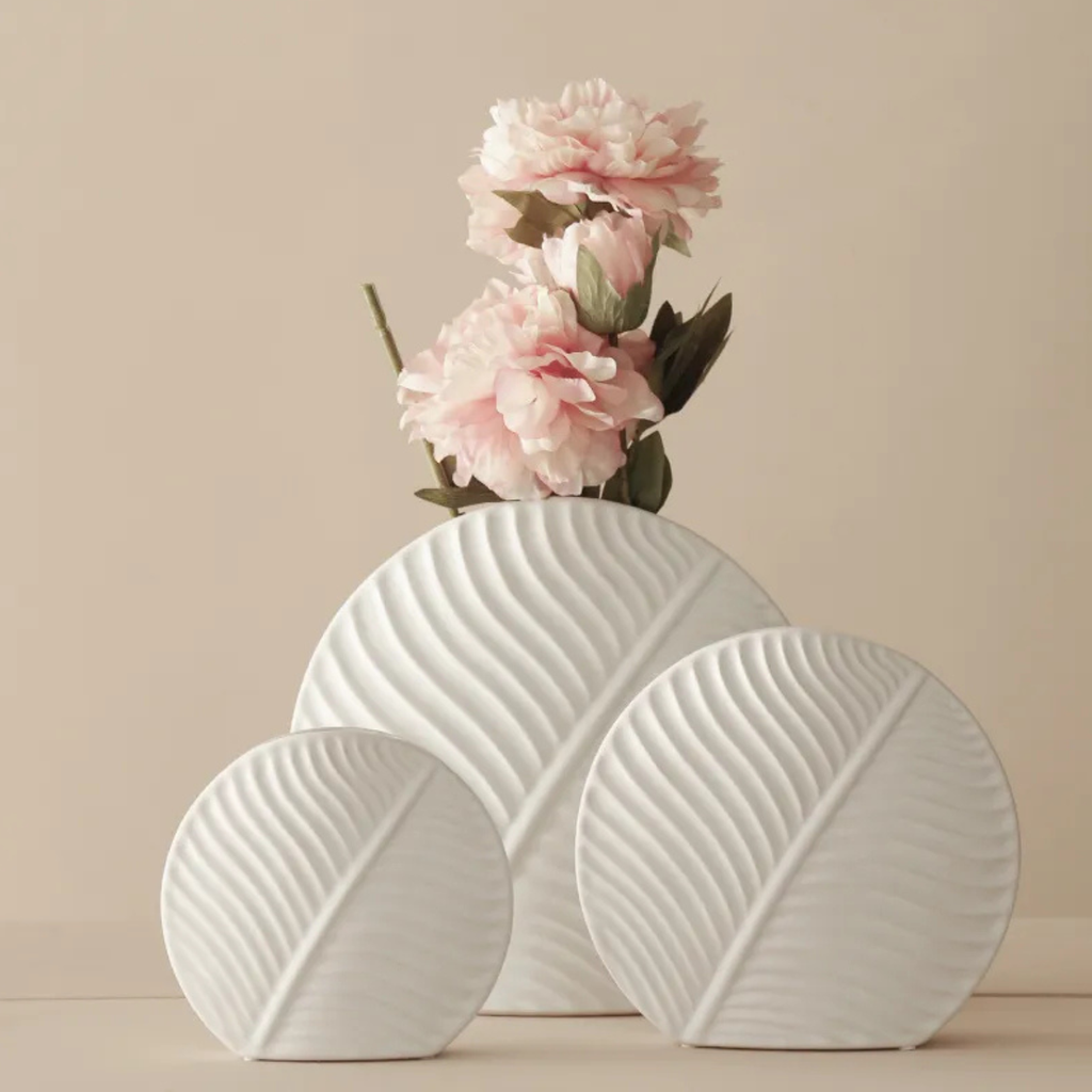 White ceramic vase with wavy design holding pink flowers on a beige background
