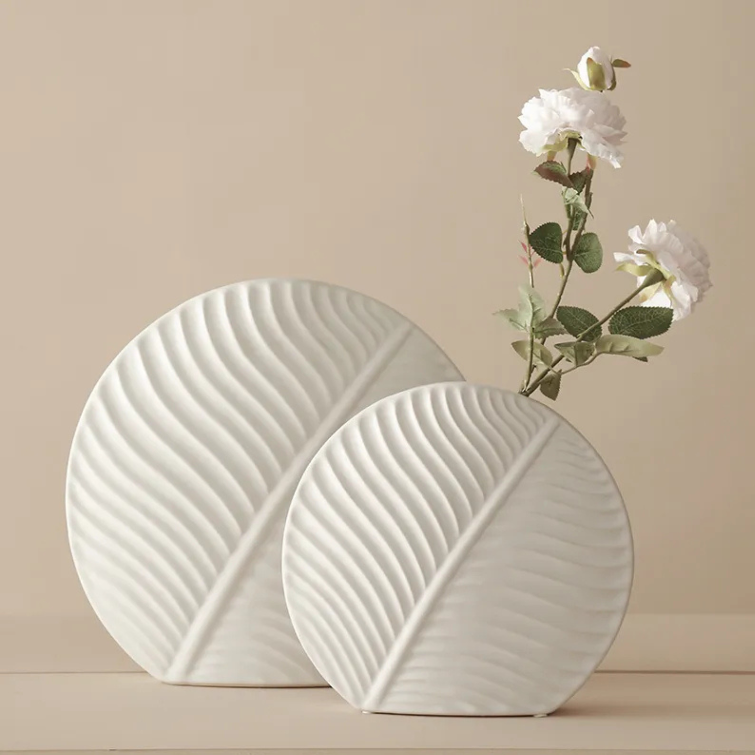 Two white ceramic vases with wavy texture on a beige surface.