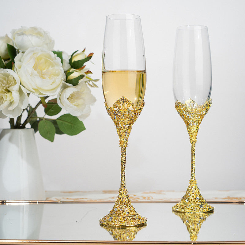 Two gold-embellished champagne flutes with white wine, next to a vase of white flowers on a reflective surface.