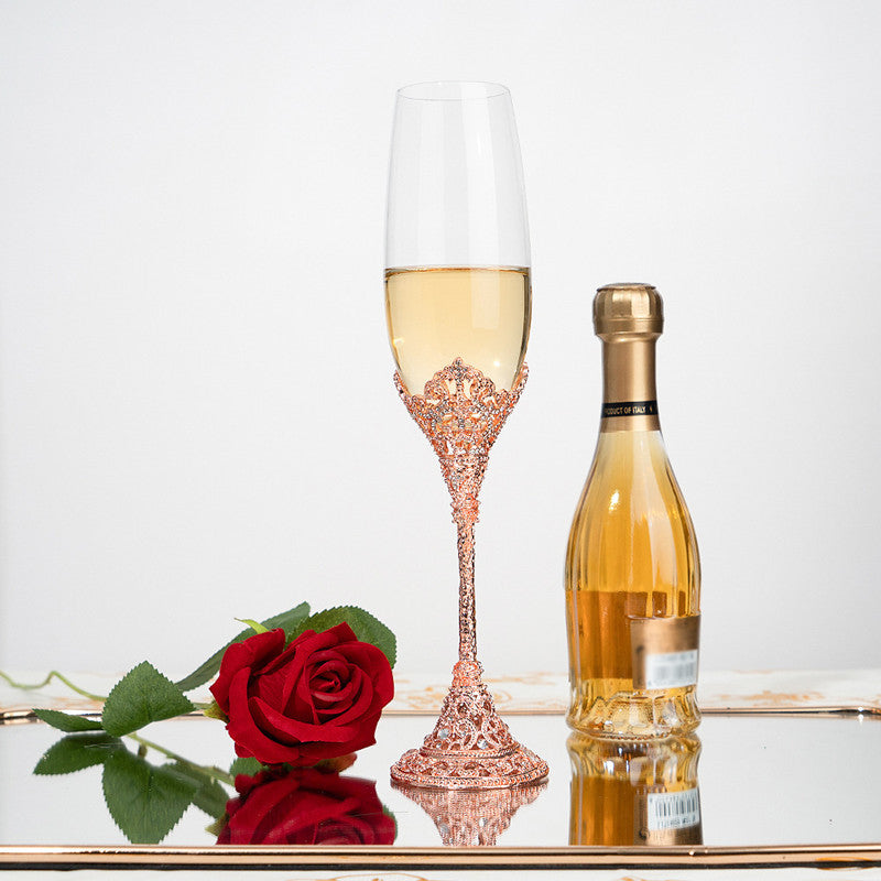 Rose gold champagne flute with white wine, bottle of white wine, and red rose on a reflective surface.